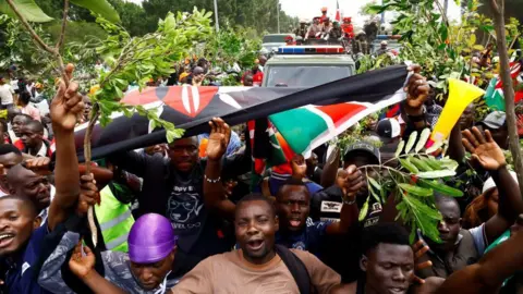 Reuters Mourners carrying twigs and palm branches hold a Kenyan flag as they escort a military vehicle
